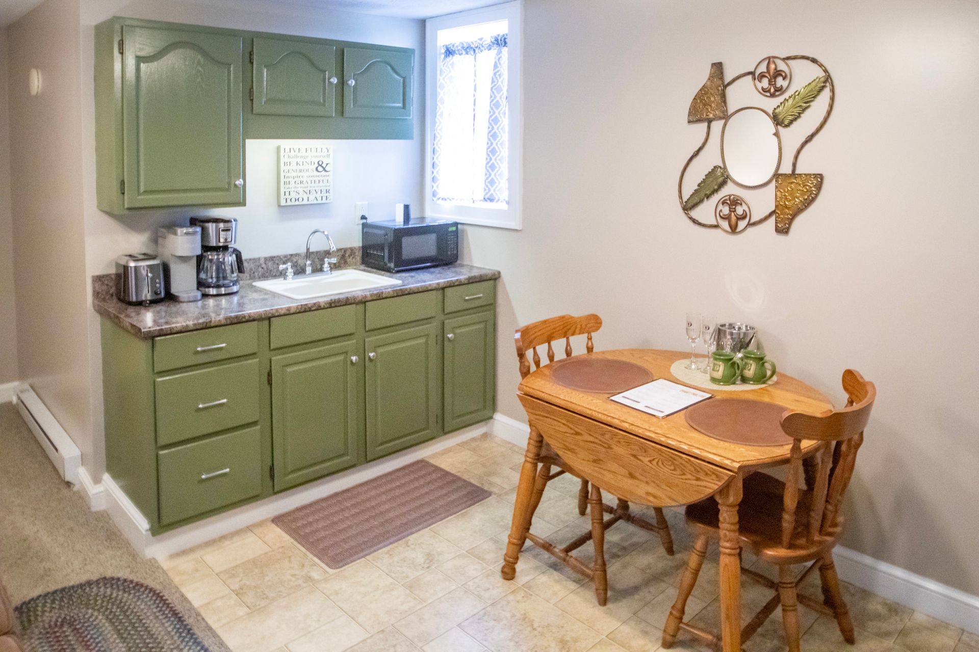 Small kitchen with green cabinets, sink, microwave, and a small wooden dining table.