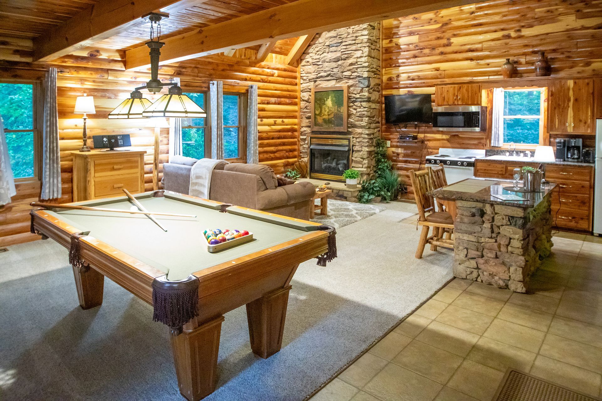Log cabin interior with a pool table, fireplace, and kitchen.