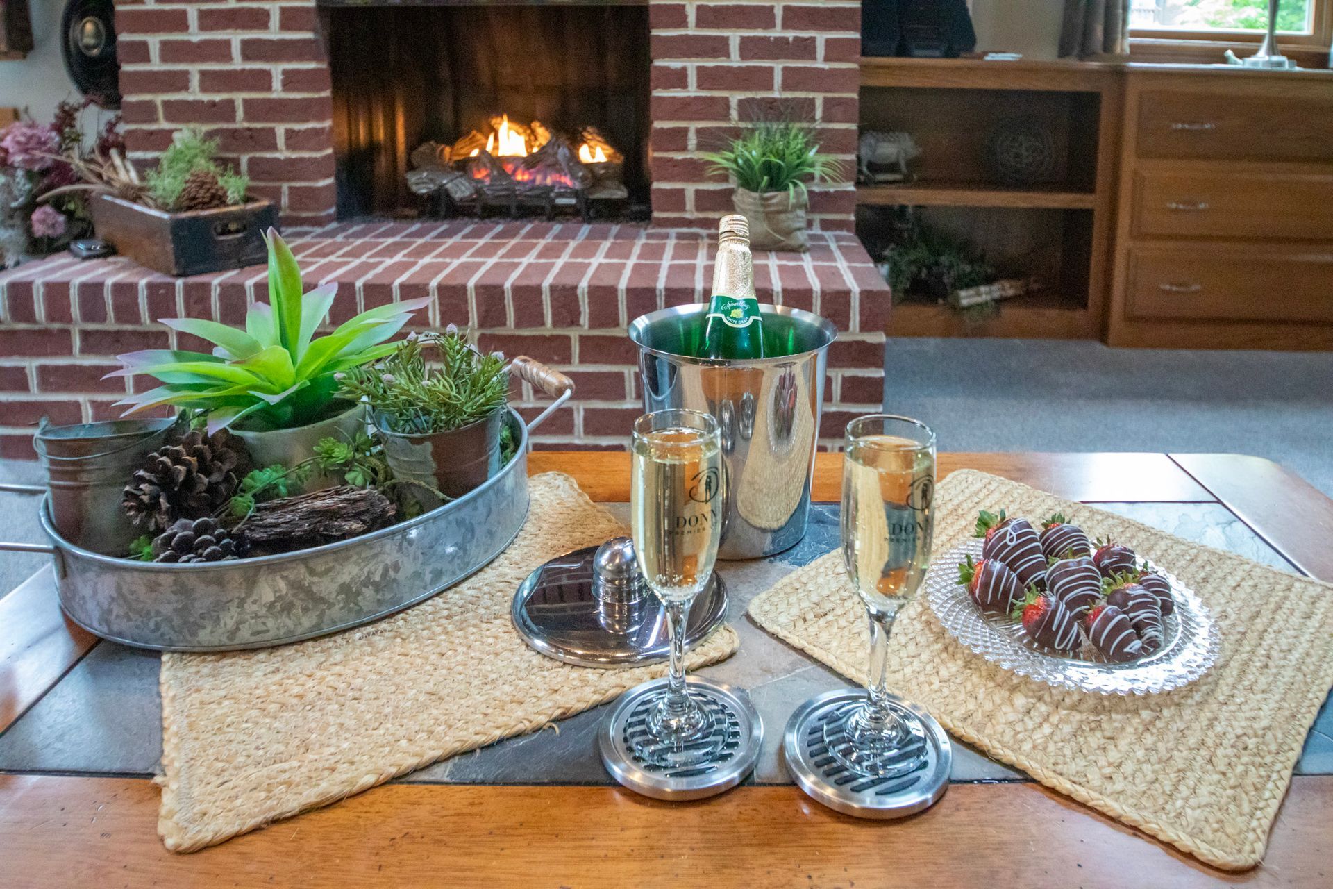 Champagne flutes, chocolate-covered strawberries, and succulents set for a celebration near a fireplace.