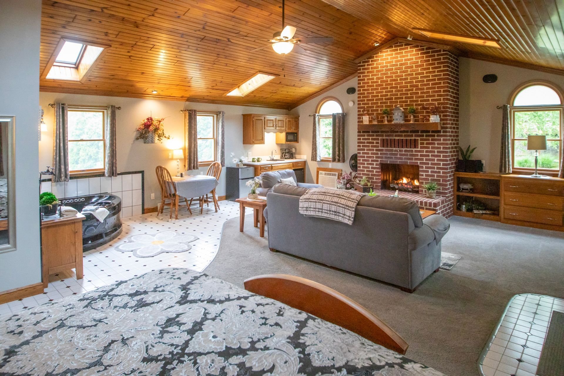 Living room with wooden ceiling, fireplace, and gray sofa. Kitchen and dining area visible.