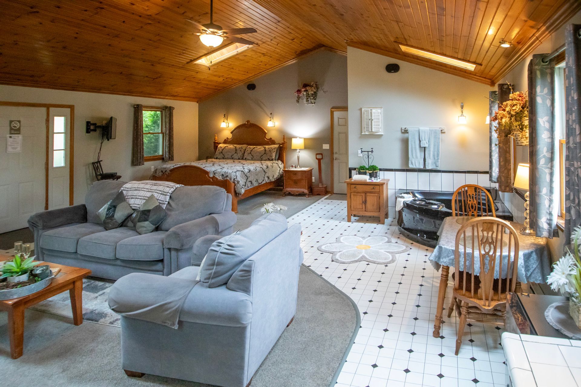 Cozy studio apartment with a bed, sofa, dining table, and wood-paneled ceiling.