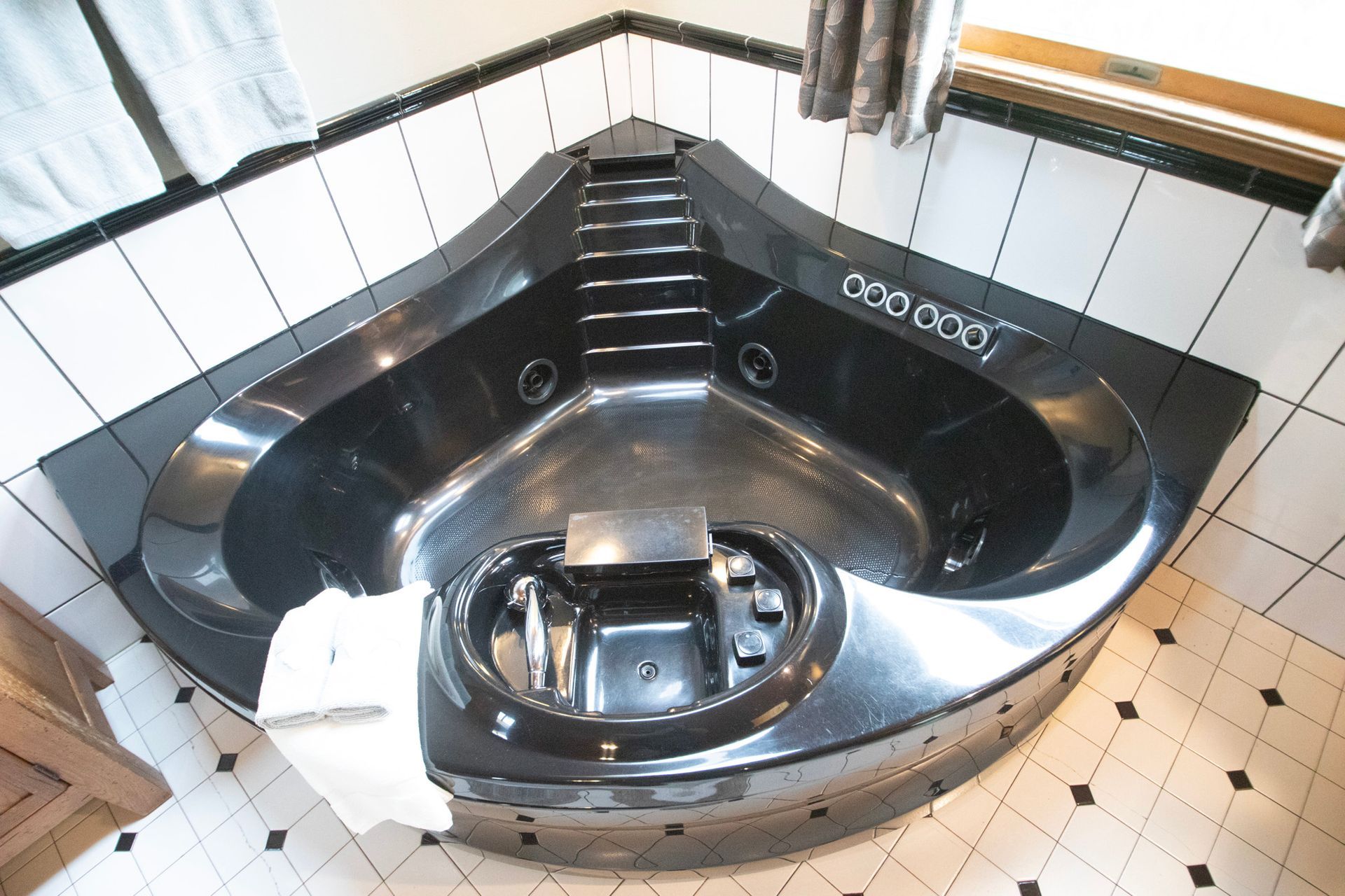 Black corner jacuzzi in a tiled bathroom.