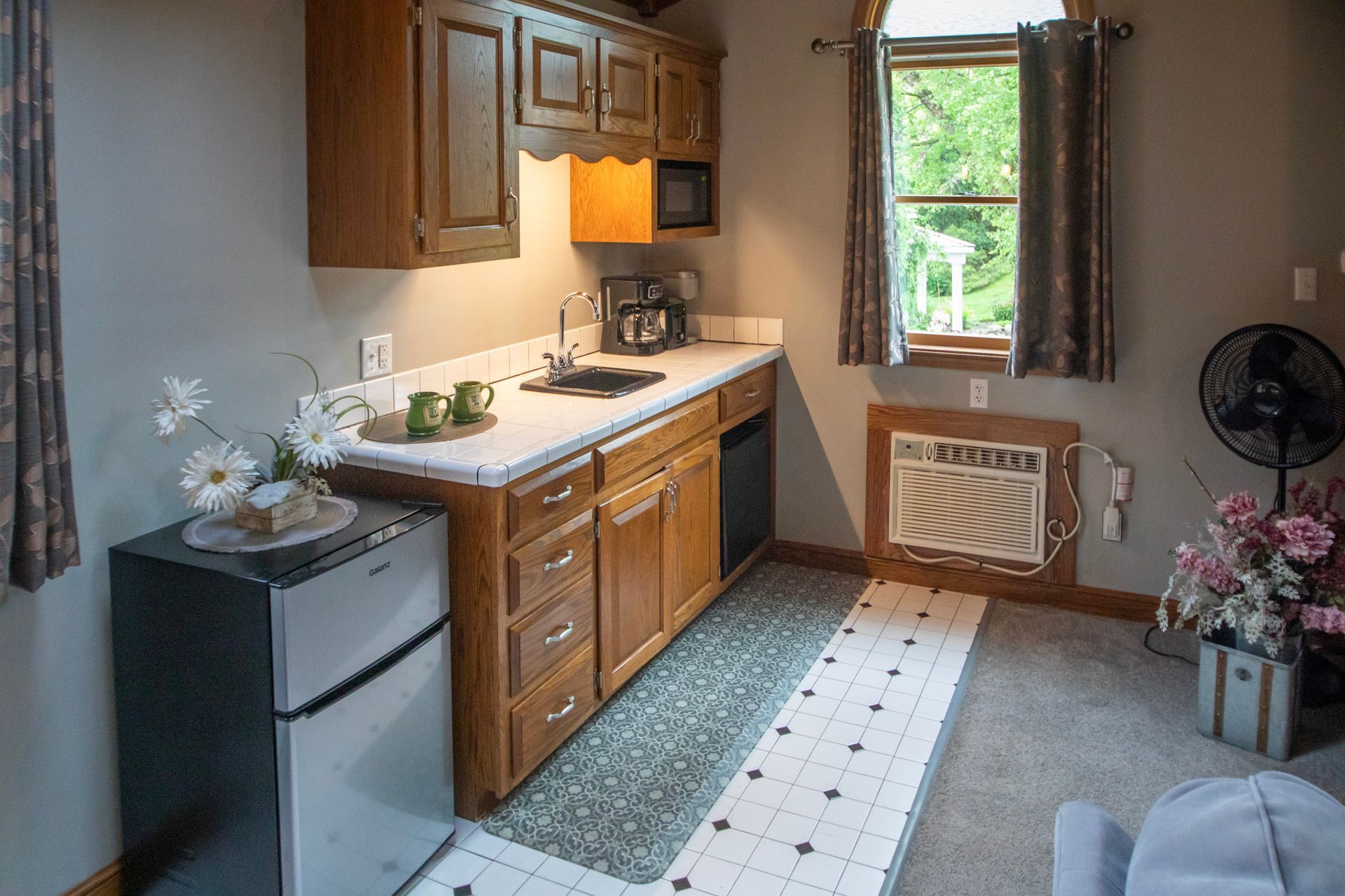 Small kitchenette with wooden cabinets, refrigerator, microwave, and a small rug.