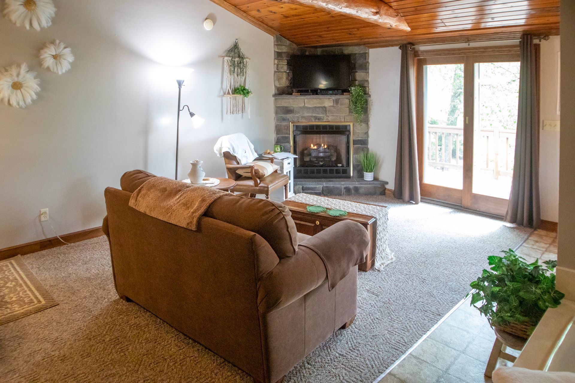 Cozy living room with fireplace, brown couch, light gray walls, and wood ceiling.