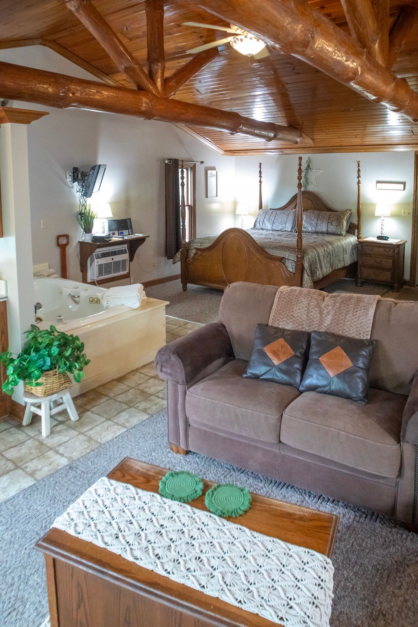 Log cabin style hotel room with a jacuzzi, four-poster bed, and a couch.