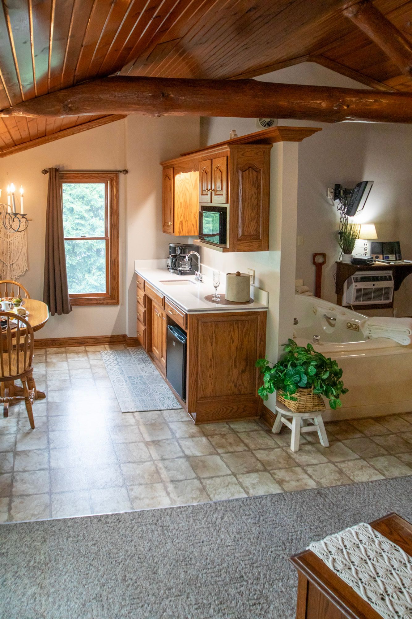 Kitchen area with wooden cabinets, counter, and appliances. Tile floor, wooden ceiling, and a window.