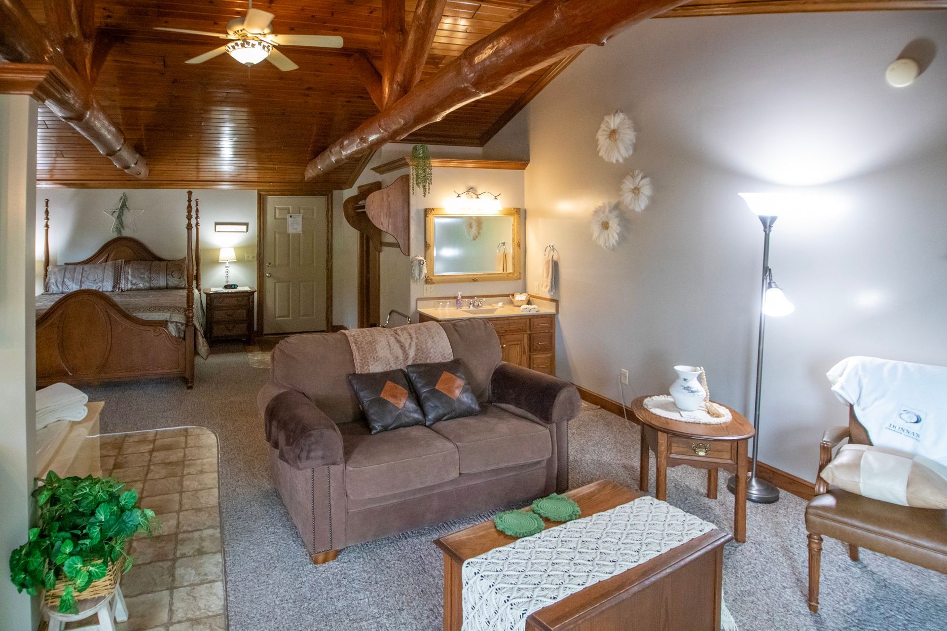 Cozy hotel room with exposed beams, sofa, bed, and sitting area. Warm colors, natural light.
