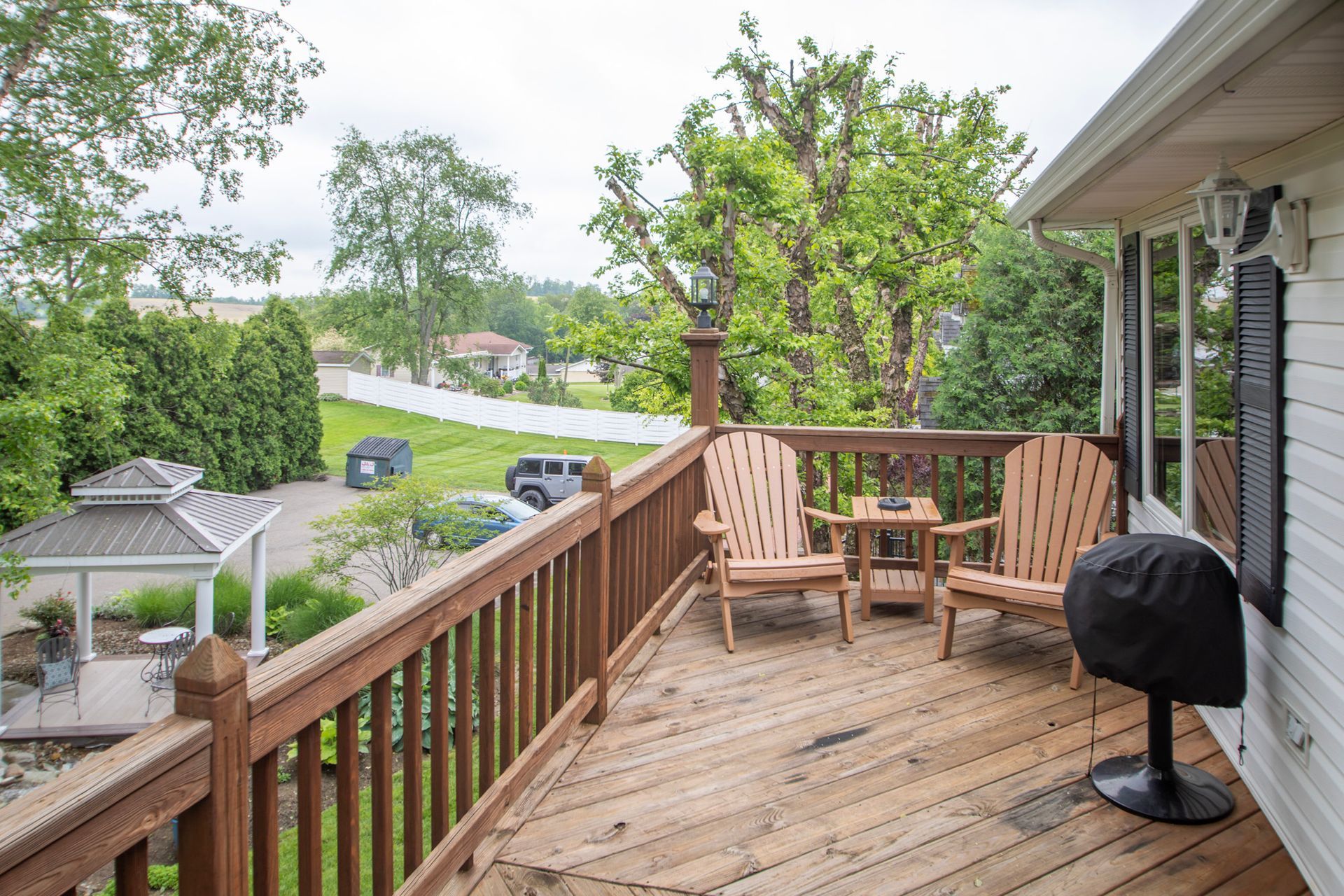 Wooden deck with two Adirondack chairs, small table, grill, and view of yard.