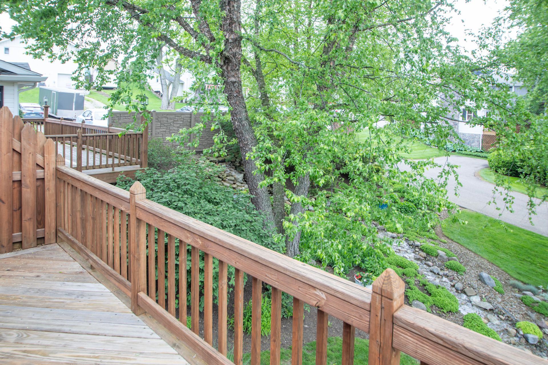 Wooden deck with railing overlooking a tree and road.
