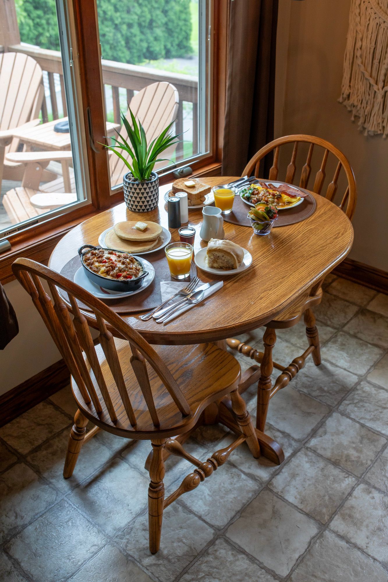 Breakfast table set near a window with food, juice, and two wooden chairs.