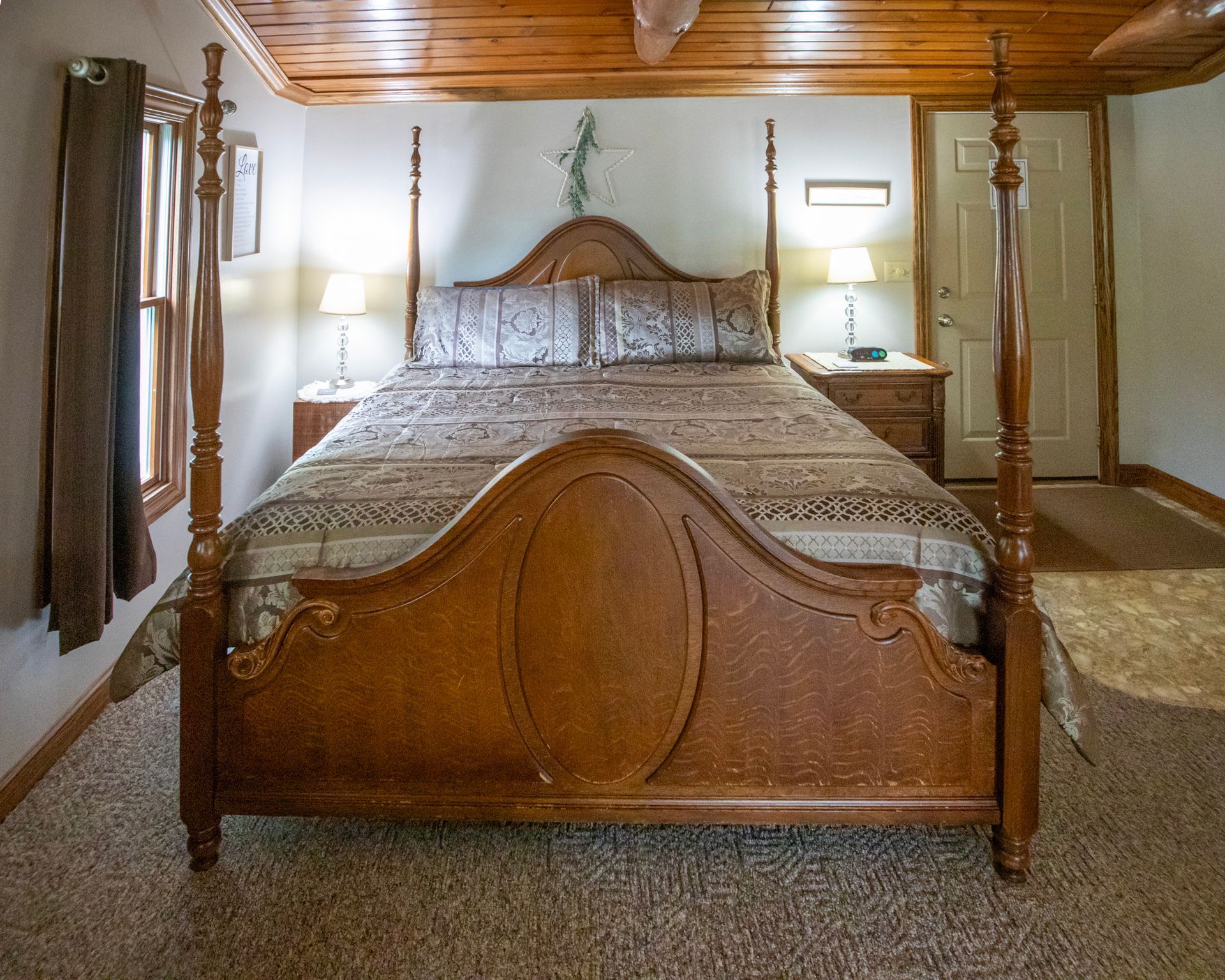 Wooden four-poster bed with floral bedding, bedside lamps, and a wooden ceiling in a bedroom.