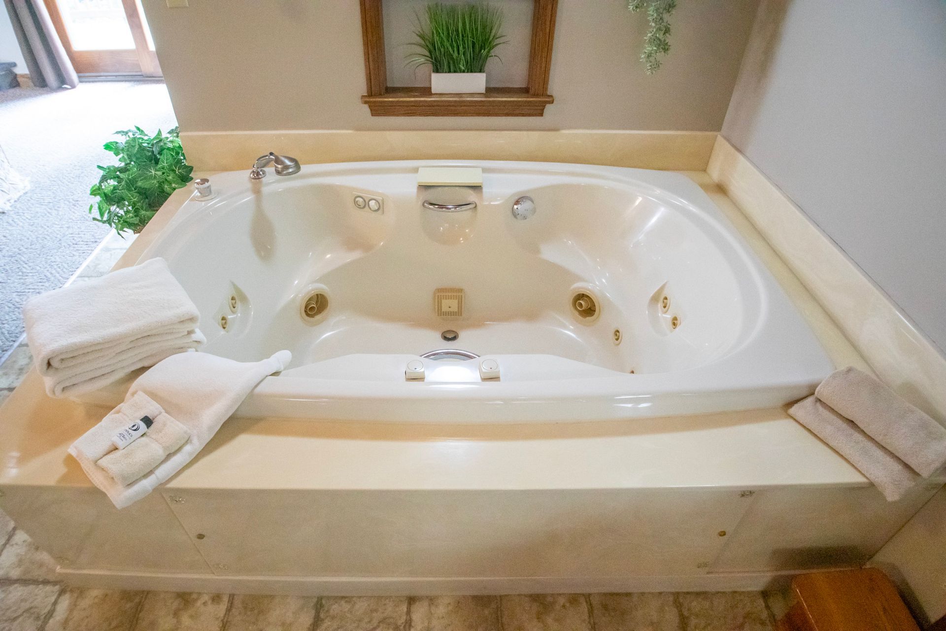 White jacuzzi tub in a room, with towels, on a stone base, beneath a shelf with a plant.