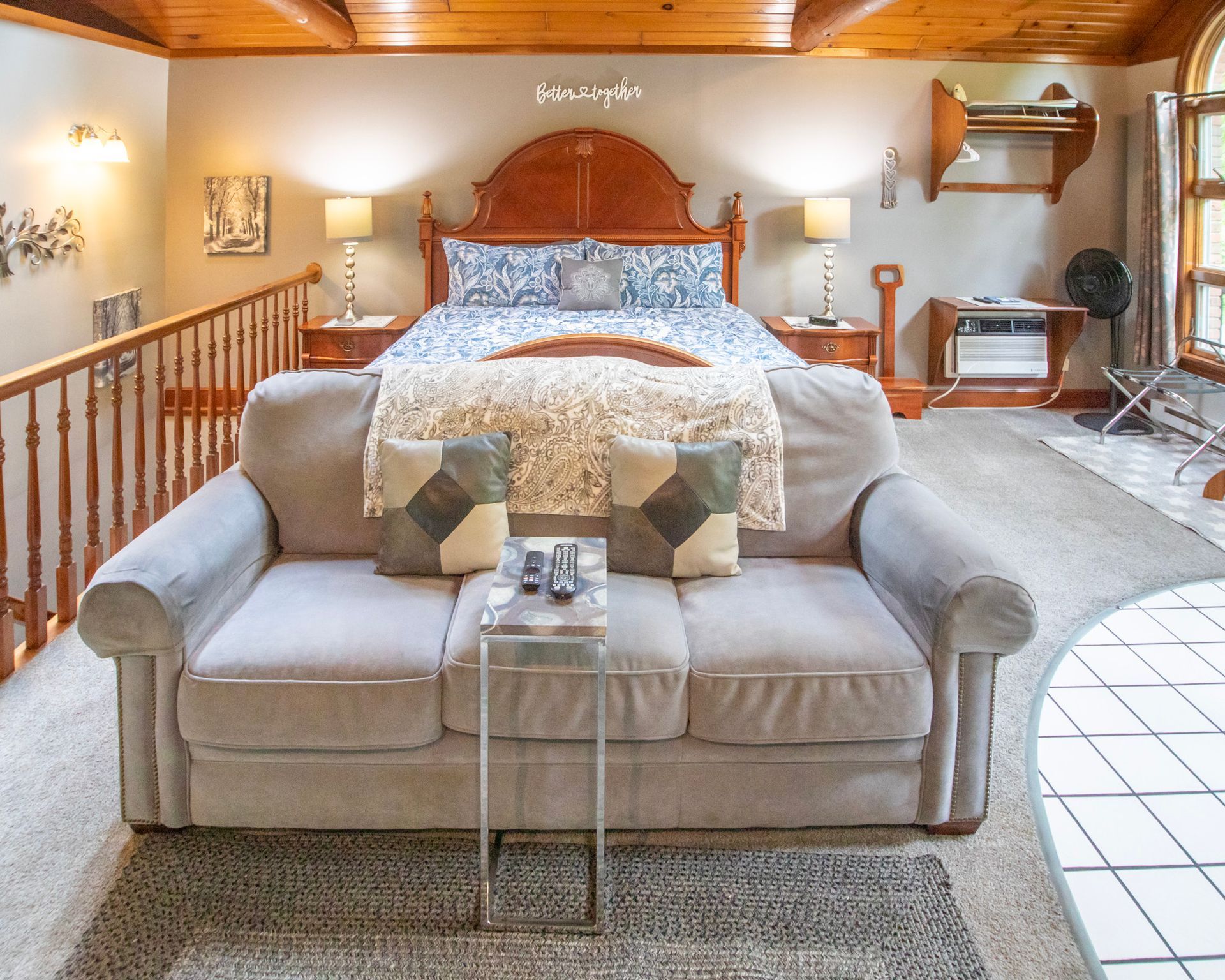 Cozy bedroom with a bed, couch, nightstands, and a loft area with wooden railings.