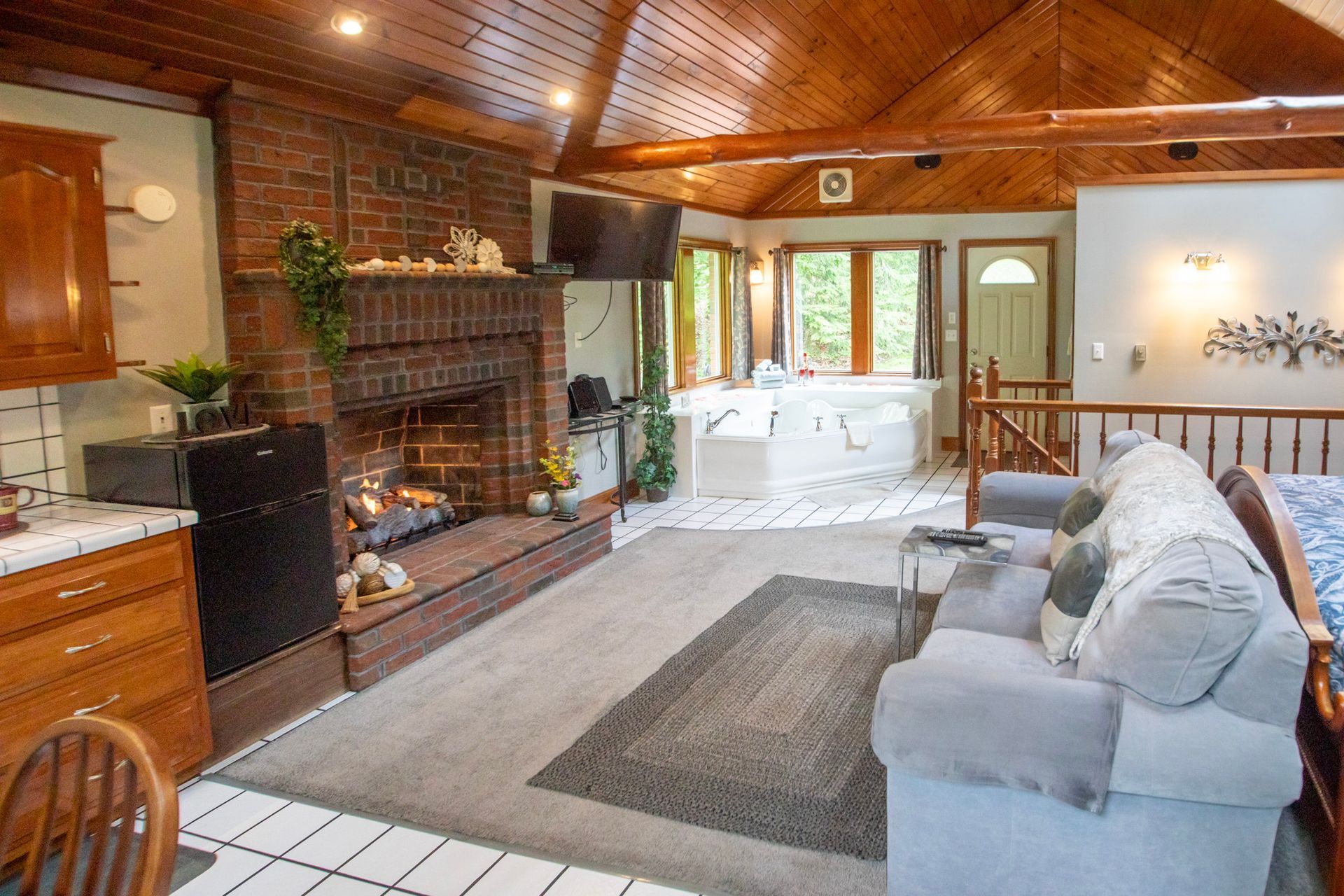 Cozy living room with brick fireplace, light gray couch, and wooden ceiling.