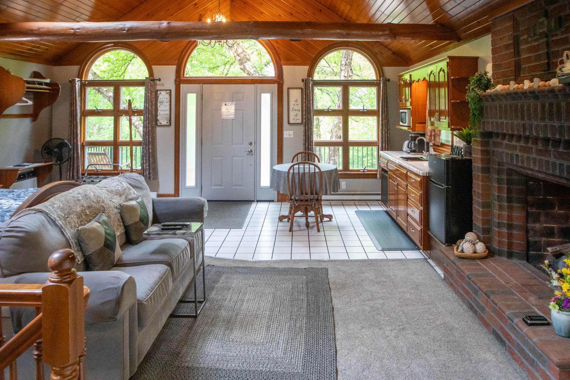 Cozy interior with arched windows, wooden ceiling, brick fireplace, and a gray sofa.