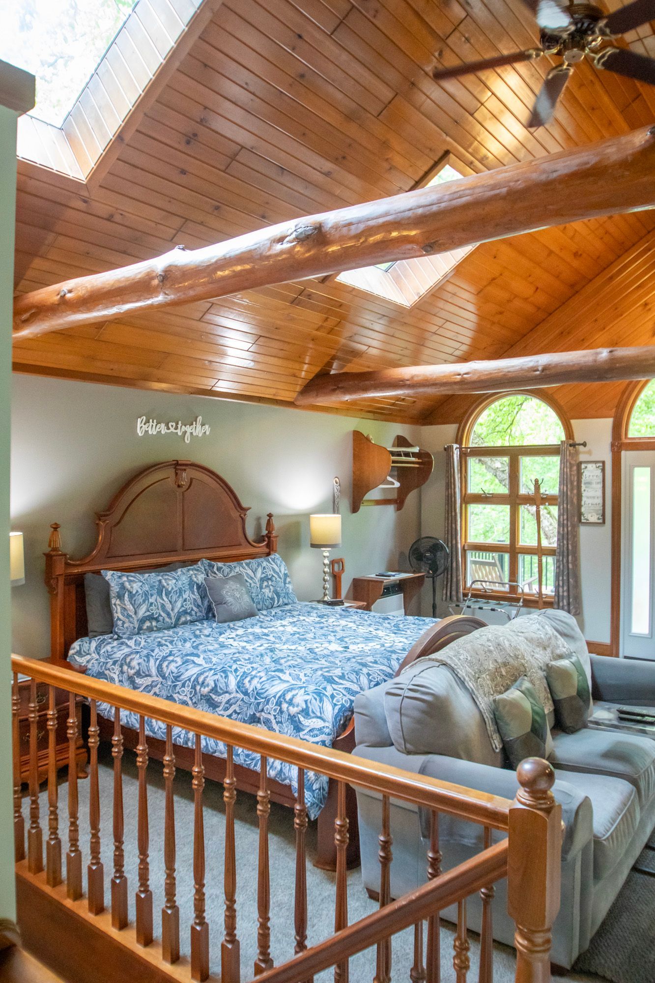 Bedroom with wooden ceiling beams, bed with blue bedding, and a gray sofa.
