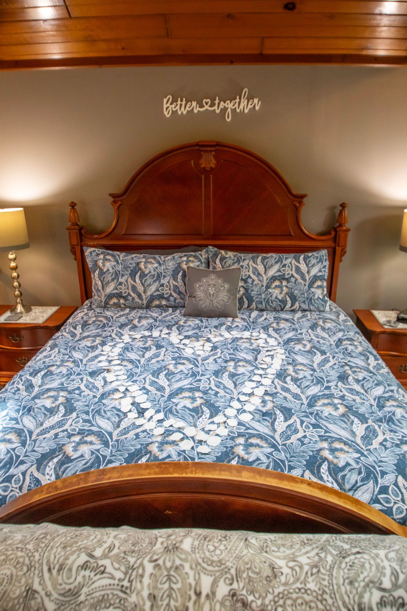 Bedroom with ornate wooden headboard, blue floral bedding, and lamps on nightstands.