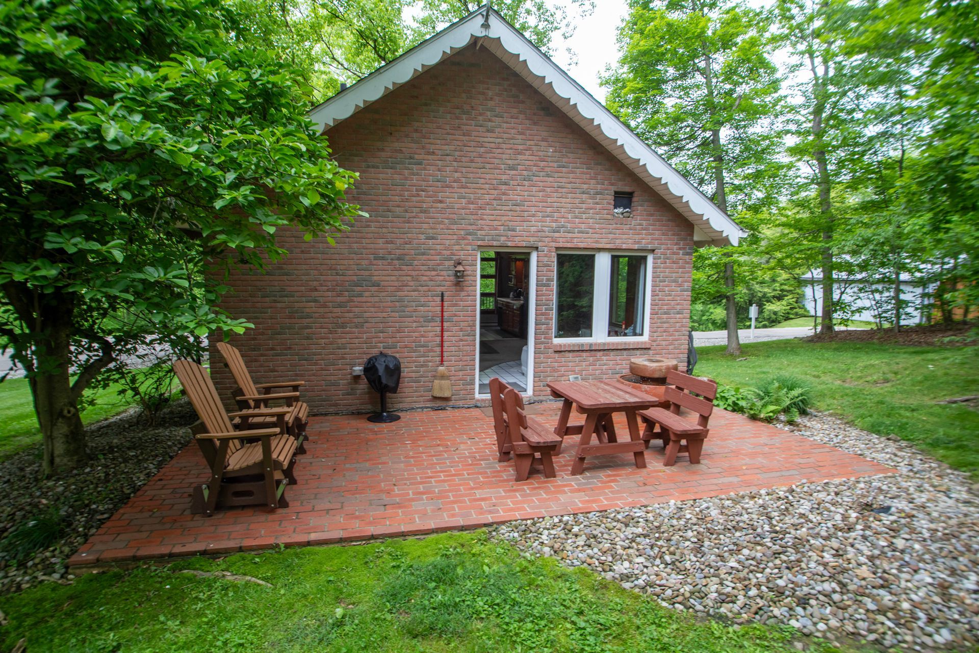 Cabin with brick siding, patio with furniture, grill, surrounded by trees and grass.