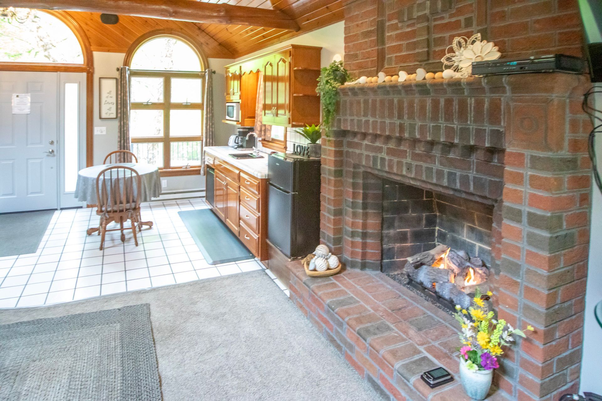 Interior kitchen with brick fireplace, table, and wooden cabinets.