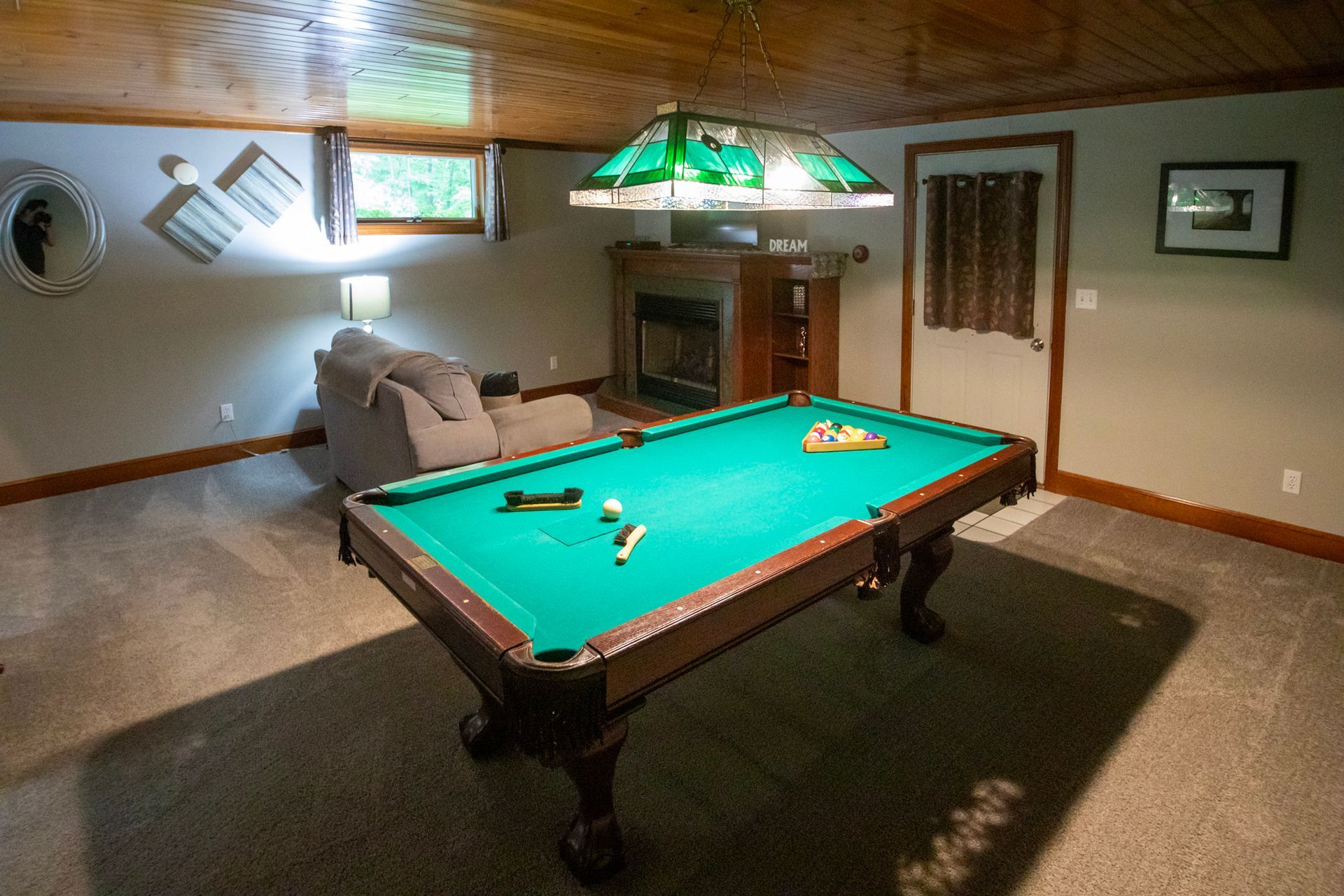 Pool table in a basement recreation room, with a fireplace, armchair, and door.