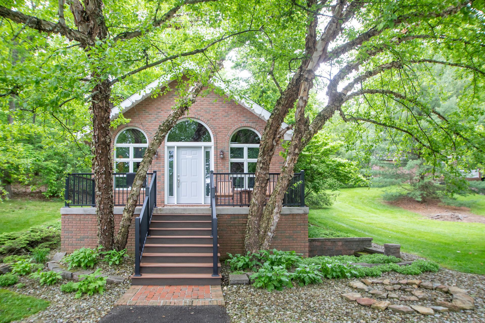 Brick cottage with arched windows, door, and stairs, nestled between trees.