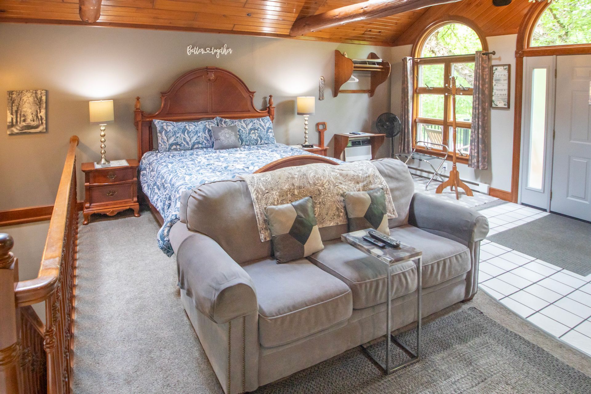 Cozy bedroom with bed, sofa, side tables, large windows, and wooden ceiling.