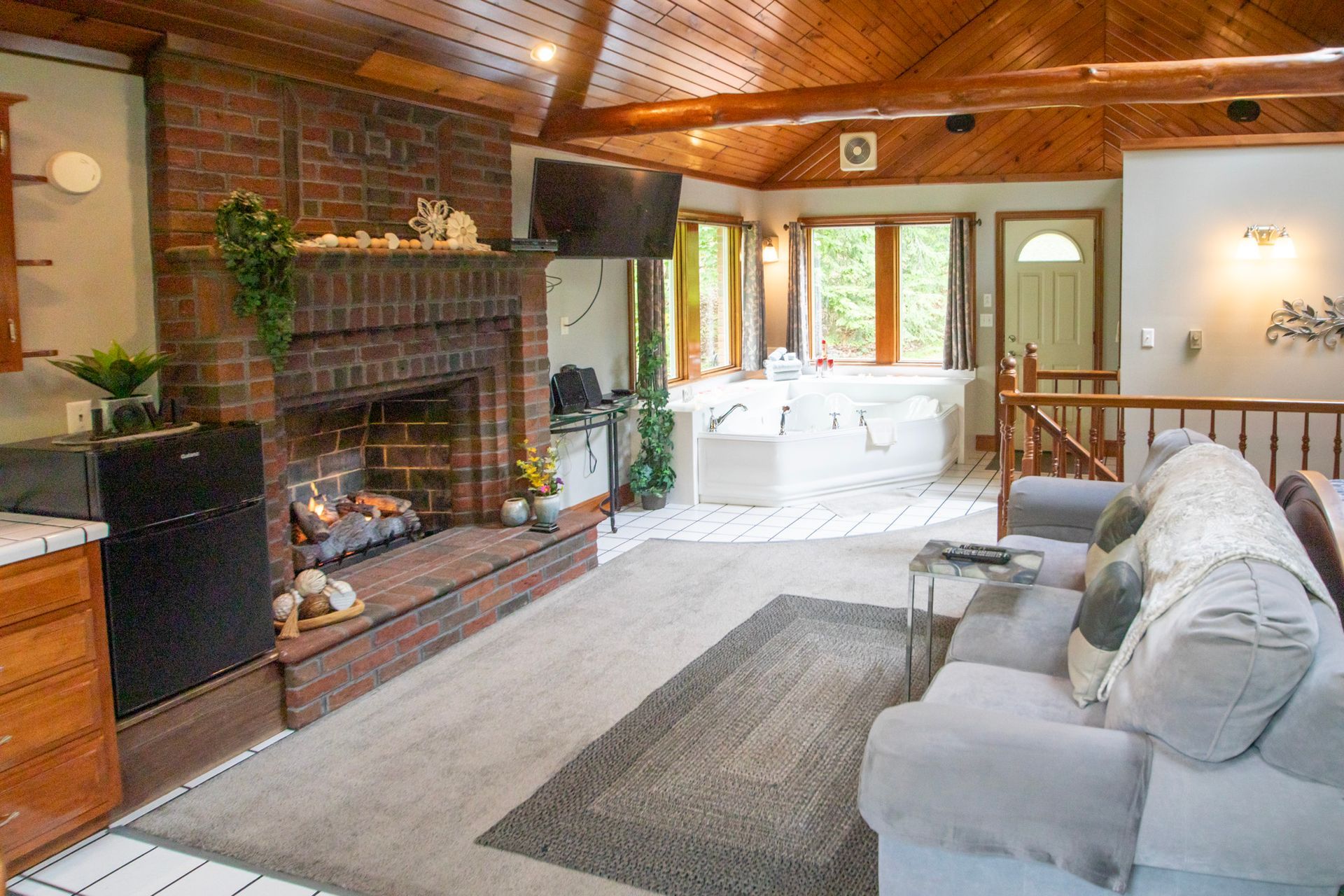 Cozy living room with brick fireplace, grey sofa, rug, and view to hot tub.