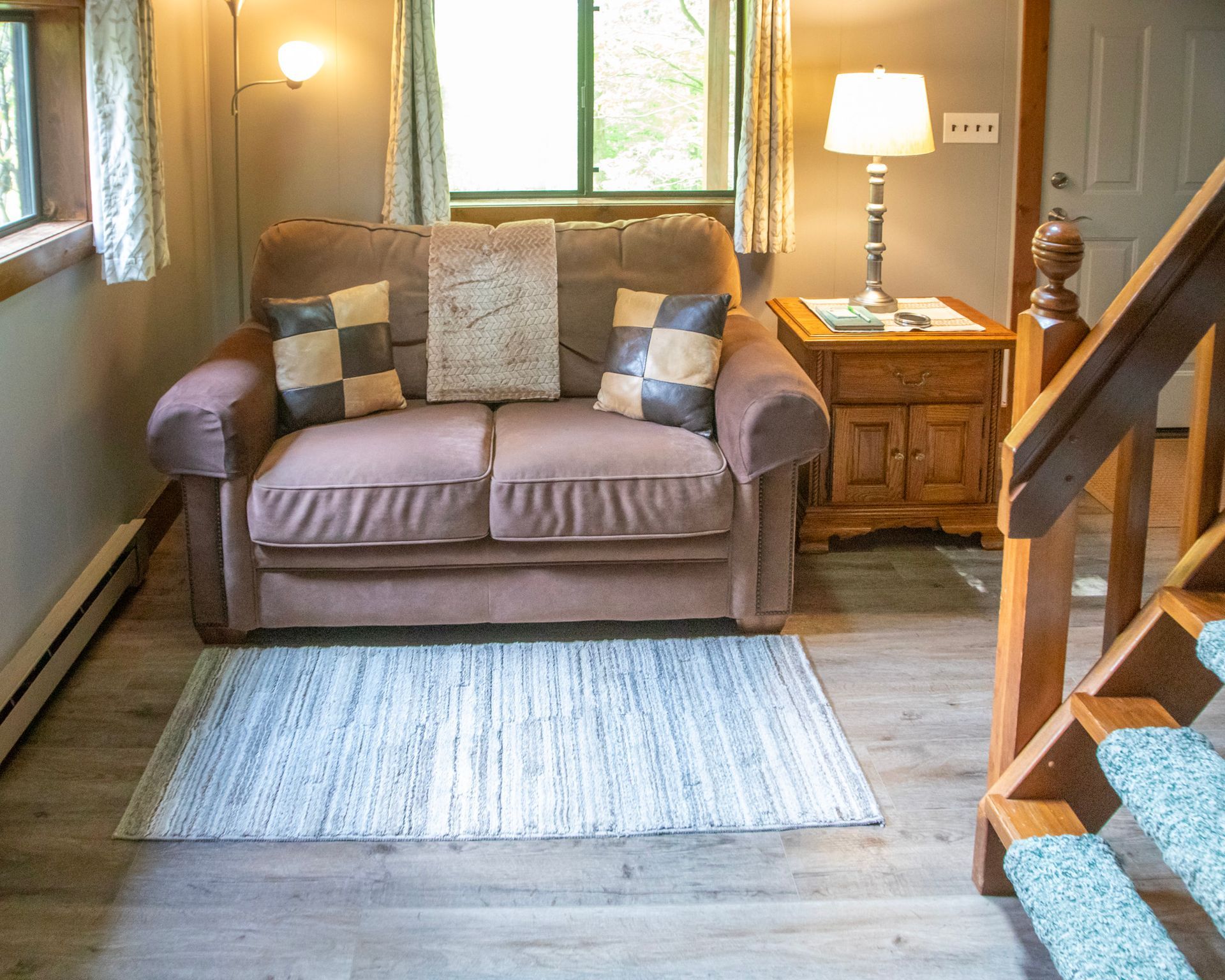 Cozy living area with a brown loveseat, rug, wooden side table, and a set of stairs.