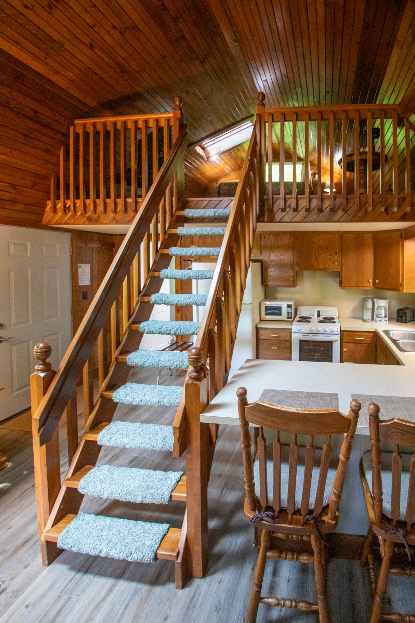 Wooden staircase leading to a loft. Interior of a cabin with kitchen and dining area visible.