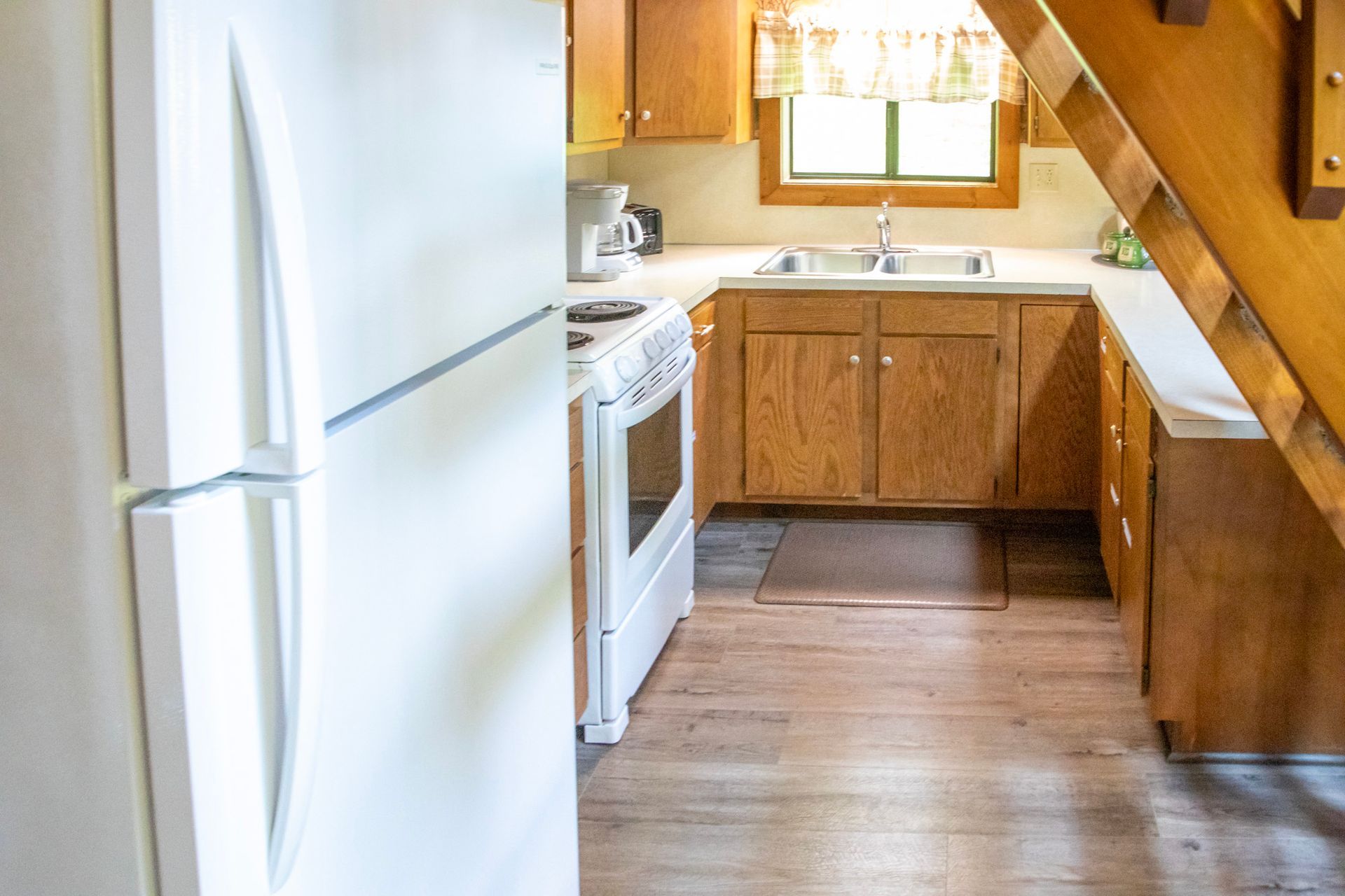 Kitchen with white appliances, wooden cabinets, and a sink under a window.