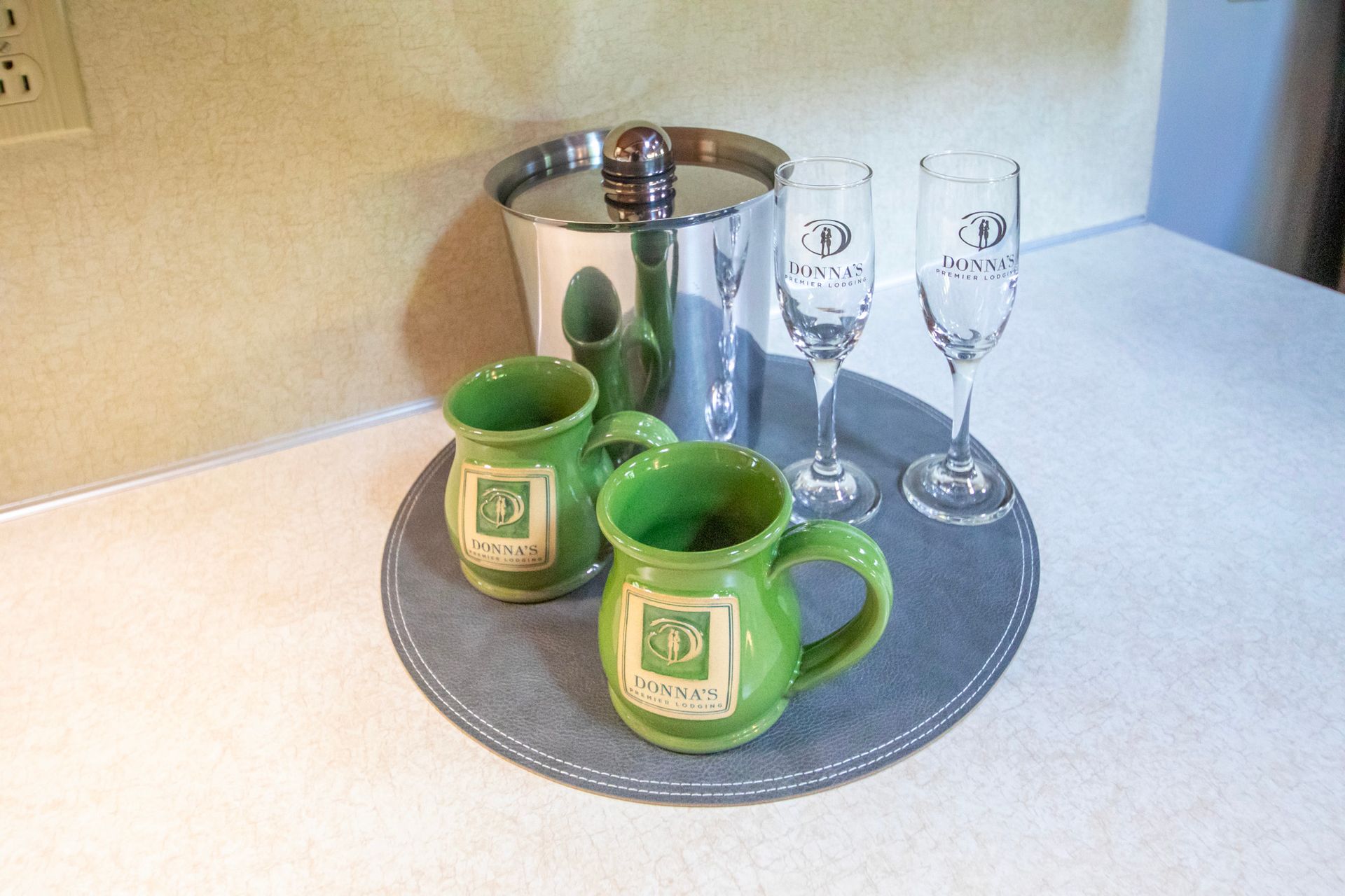 Two green mugs, champagne flutes, and ice bucket on a gray tray on a countertop.