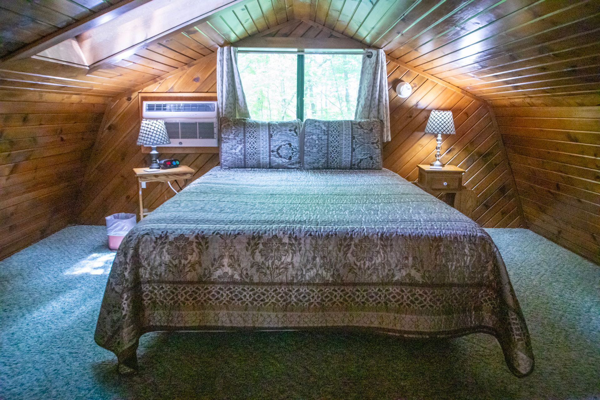 Bedroom with angled wood walls, a bed with patterned cover, two lamps on nightstands, and a window.