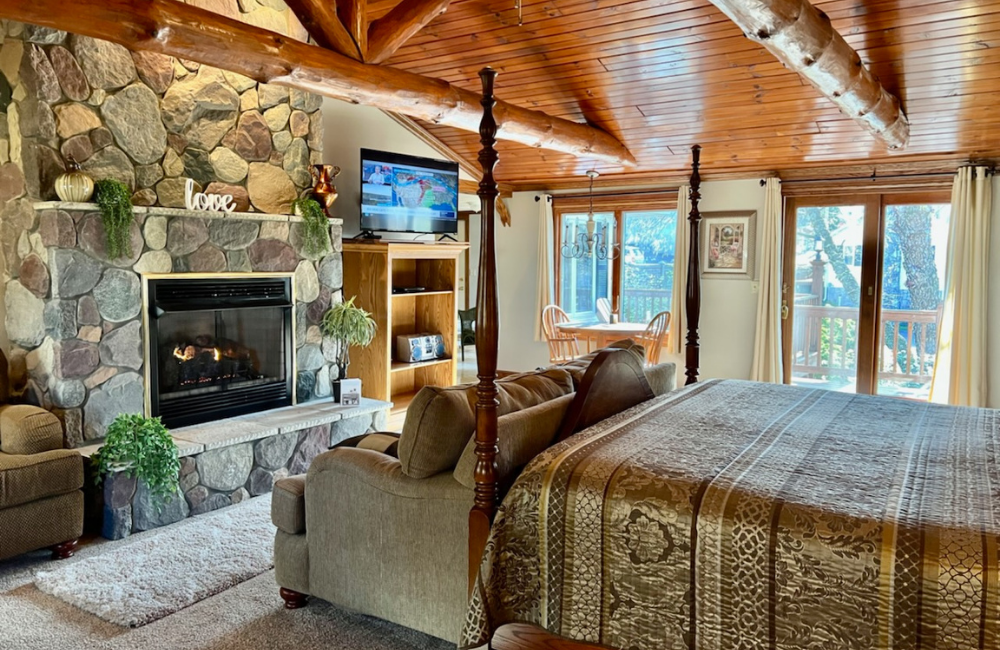 Cozy lodge-style bedroom with stone fireplace, four-poster bed, and log-beamed ceiling.