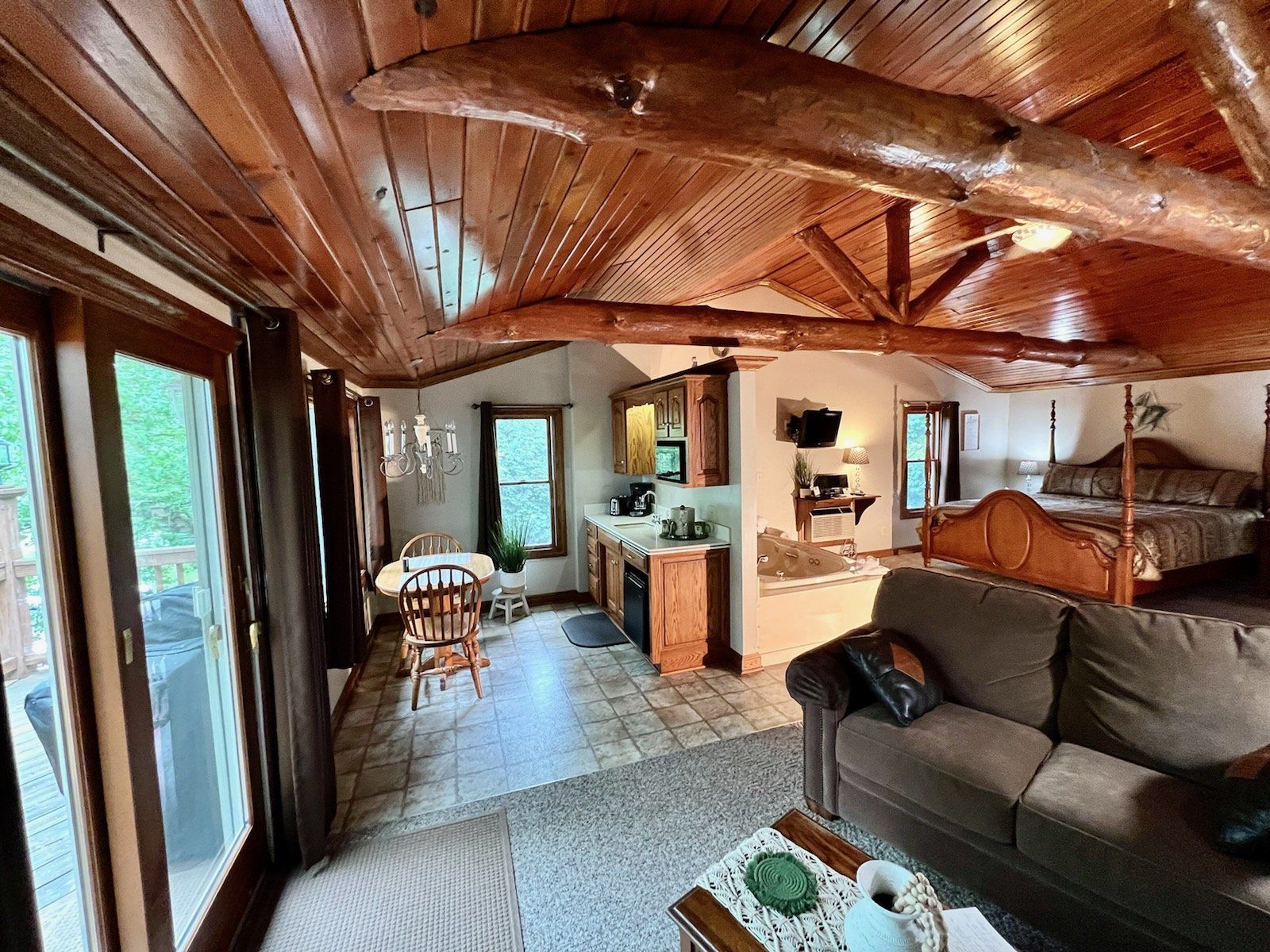 Interior of a cabin with wooden ceiling and beams, a living area, kitchen, and bed.
