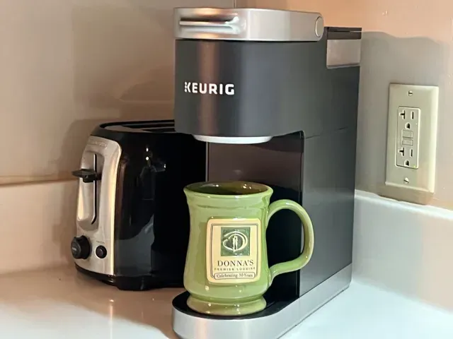 Keurig coffee maker with a green mug, next to a black toaster on a kitchen counter.
