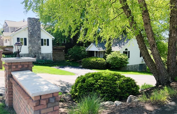 White houses with trees and brick fence. Green lawn and sunny day.