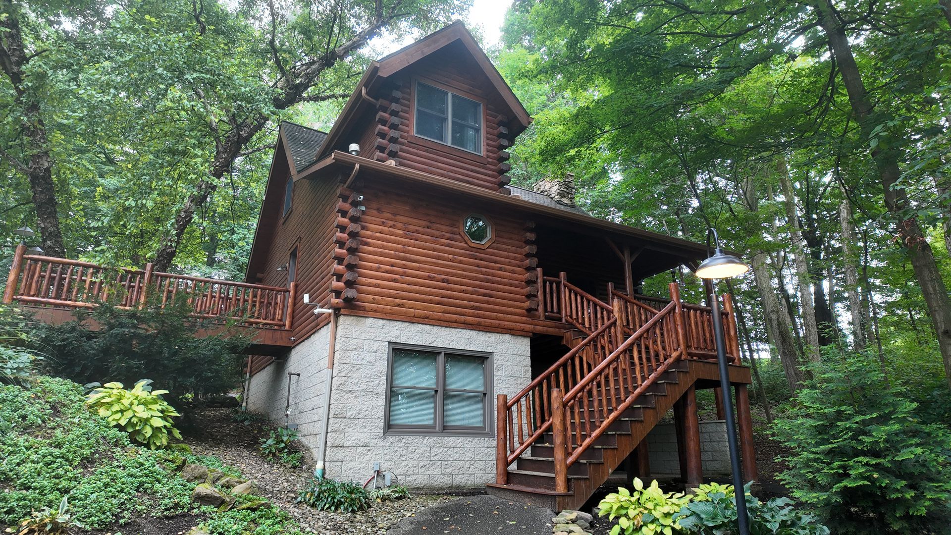 Log cabin with wooden exterior, set in lush greenery. Wooden stairs lead to entrance.