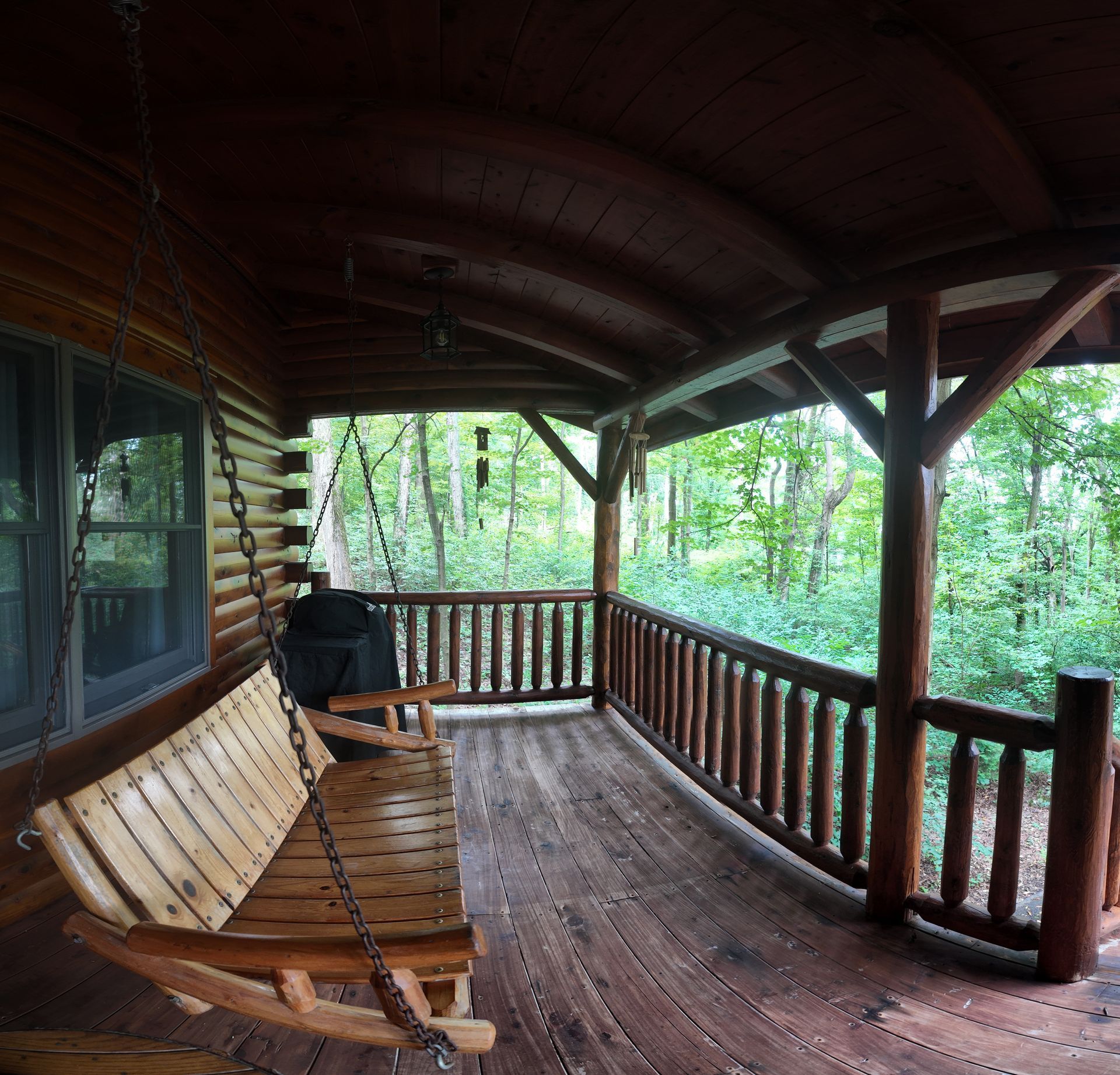 Covered porch with wooden swing, railings, and view of green trees.