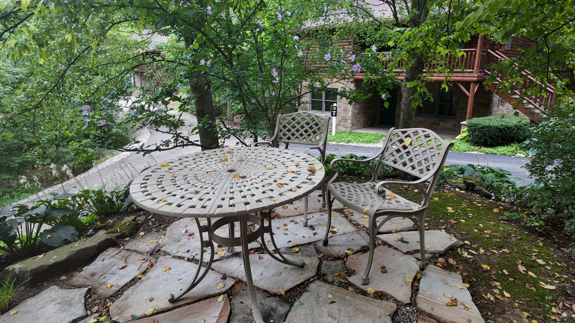 Patio with ornate white metal table and chairs, surrounded by greenery and stone pavers.