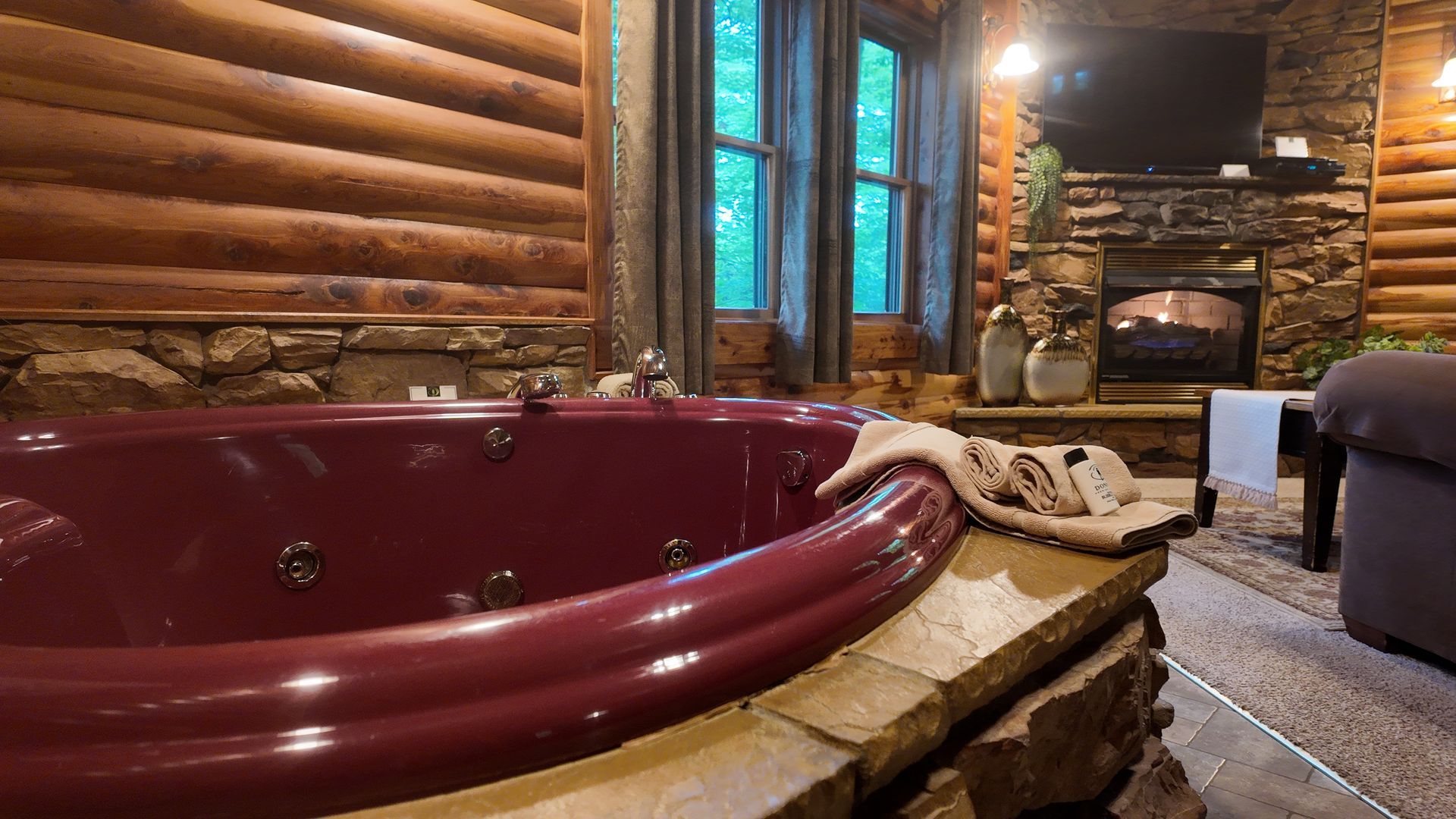 Cozy cabin interior with a burgundy hot tub, fireplace, and window overlooking trees.