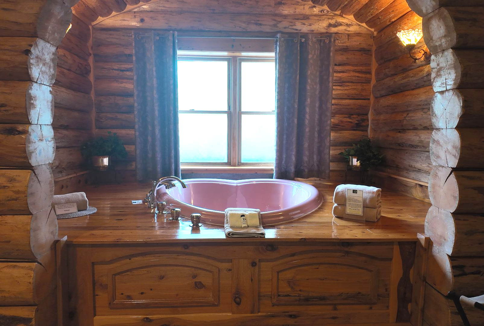 Cozy wooden bathroom with a pink jacuzzi tub, window, and blue curtains.
