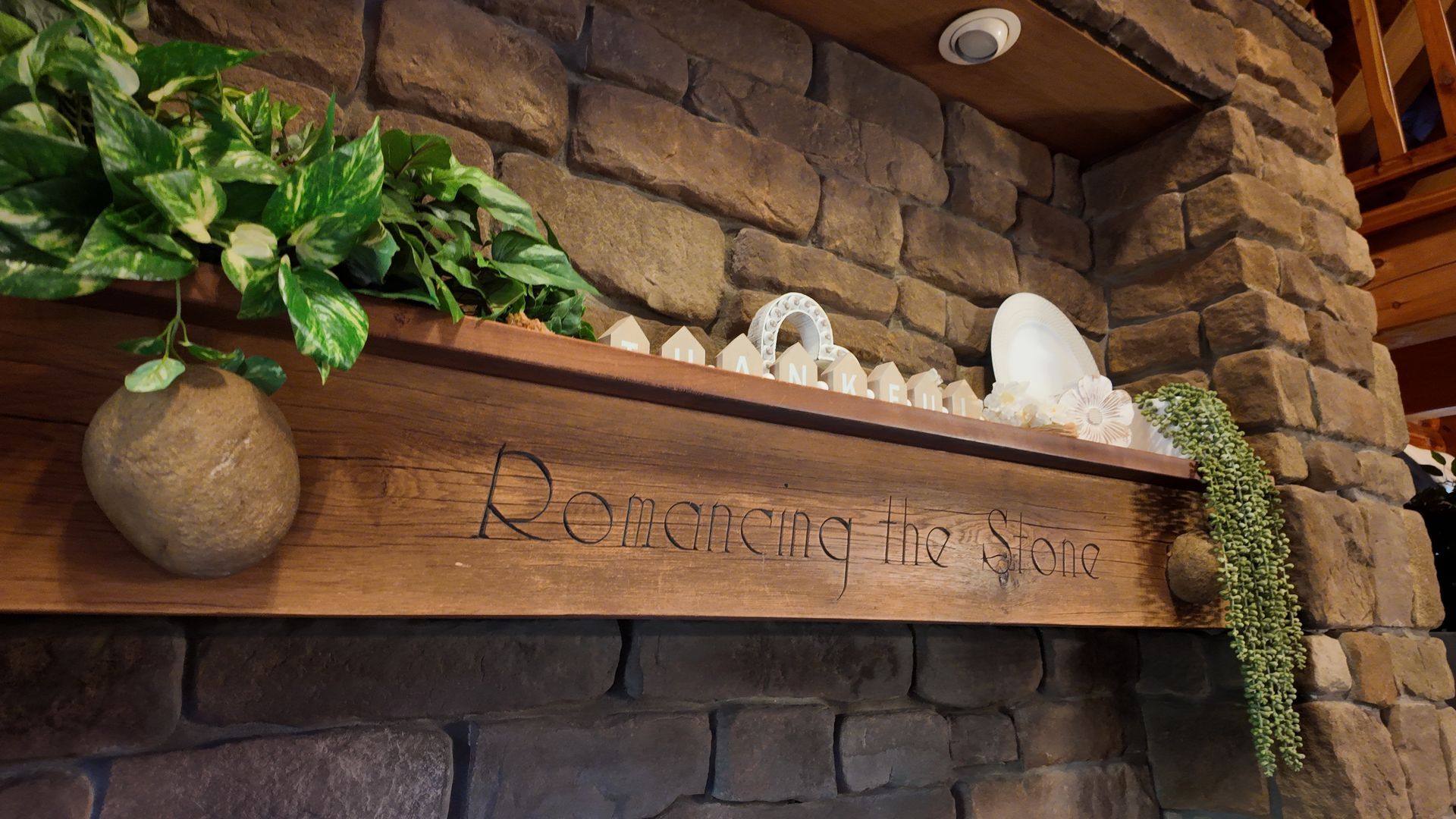 A wooden shelf with carved inscription, decorated with plants and white crystals, set against a stone wall.