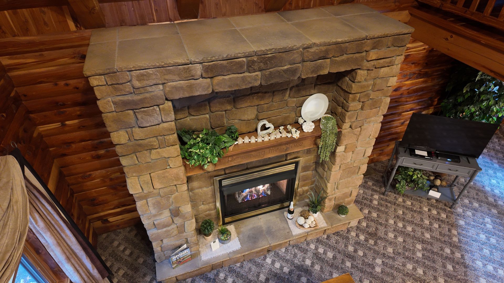 Stone fireplace in a cabin interior, decorated with plants and a 