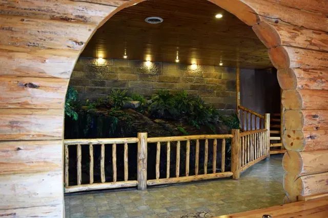 Wooden arched doorway leading to a balcony with log railing, view of stone wall and foliage.