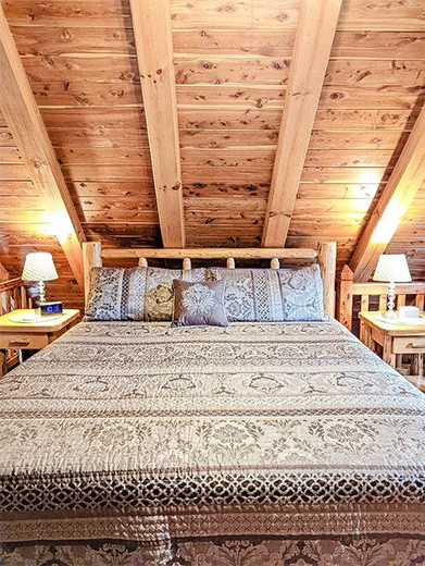 Bedroom with log-style bed, wooden ceiling, bedside tables, and lamps.