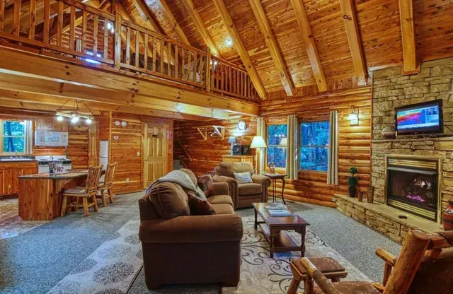 Log cabin interior with a living area, fireplace, and loft.