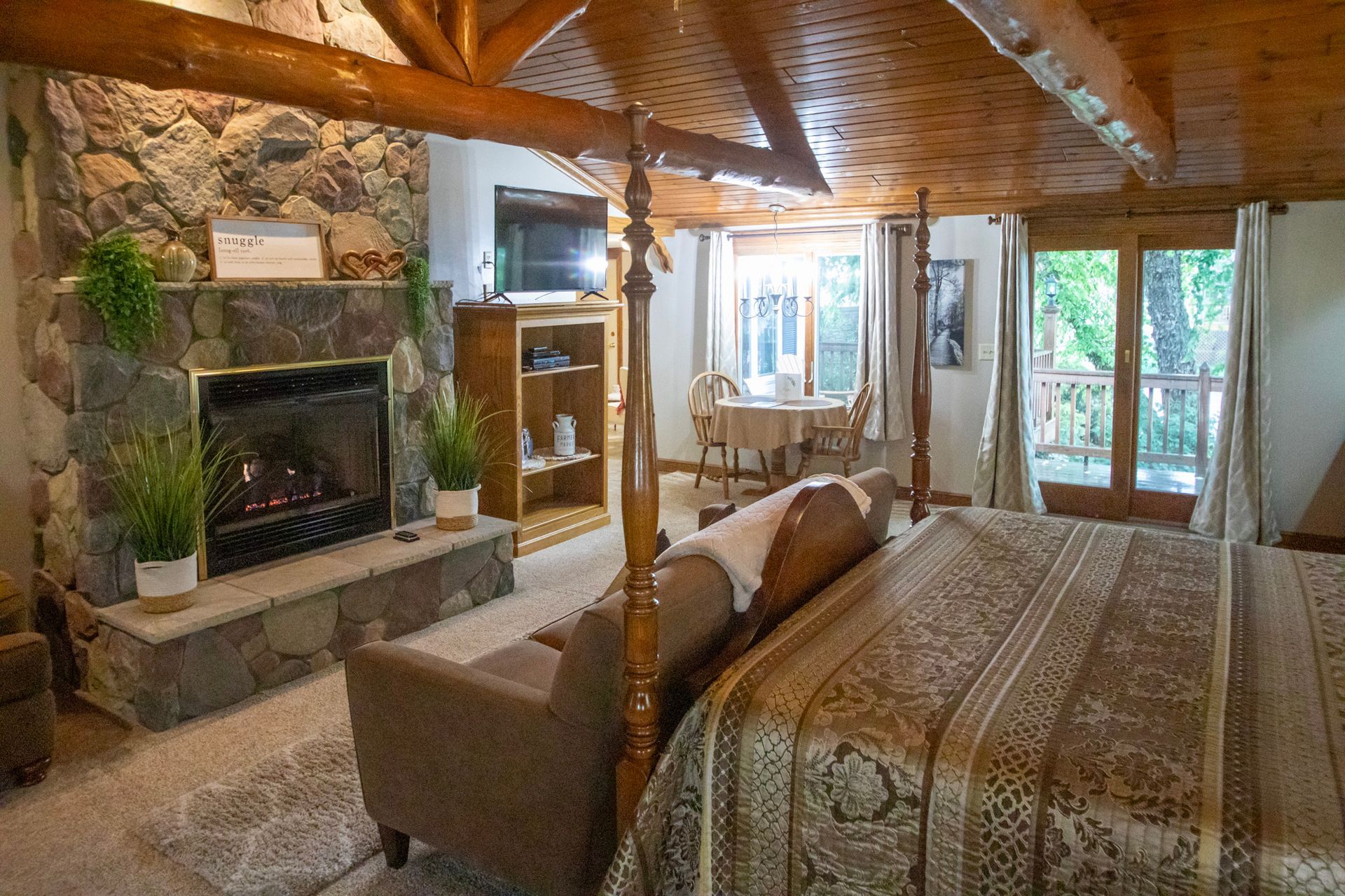 Cozy cabin interior with stone fireplace, wood beams, four-poster bed, and a couch.