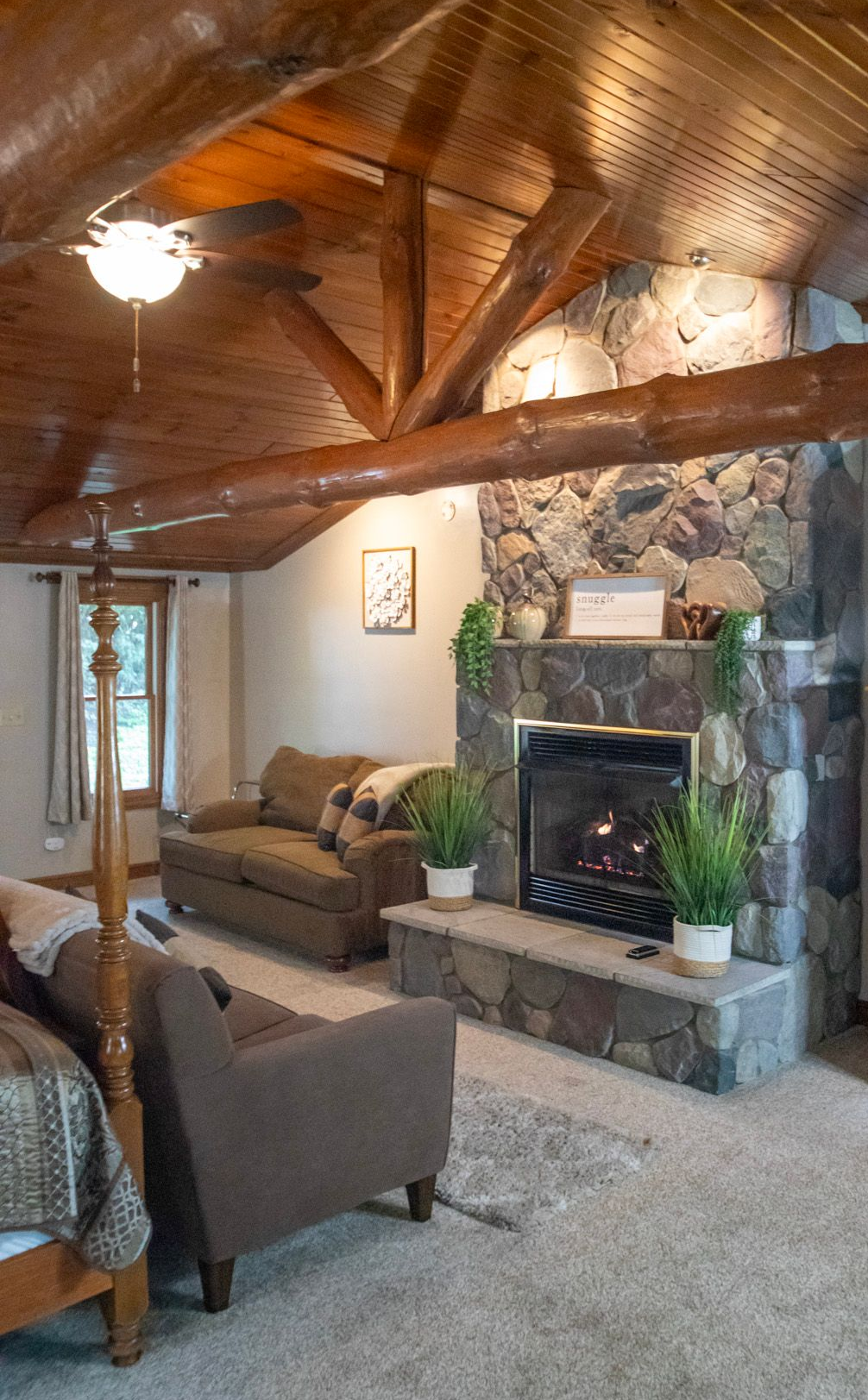 Living room with a stone fireplace, brown sofa, and log ceiling.