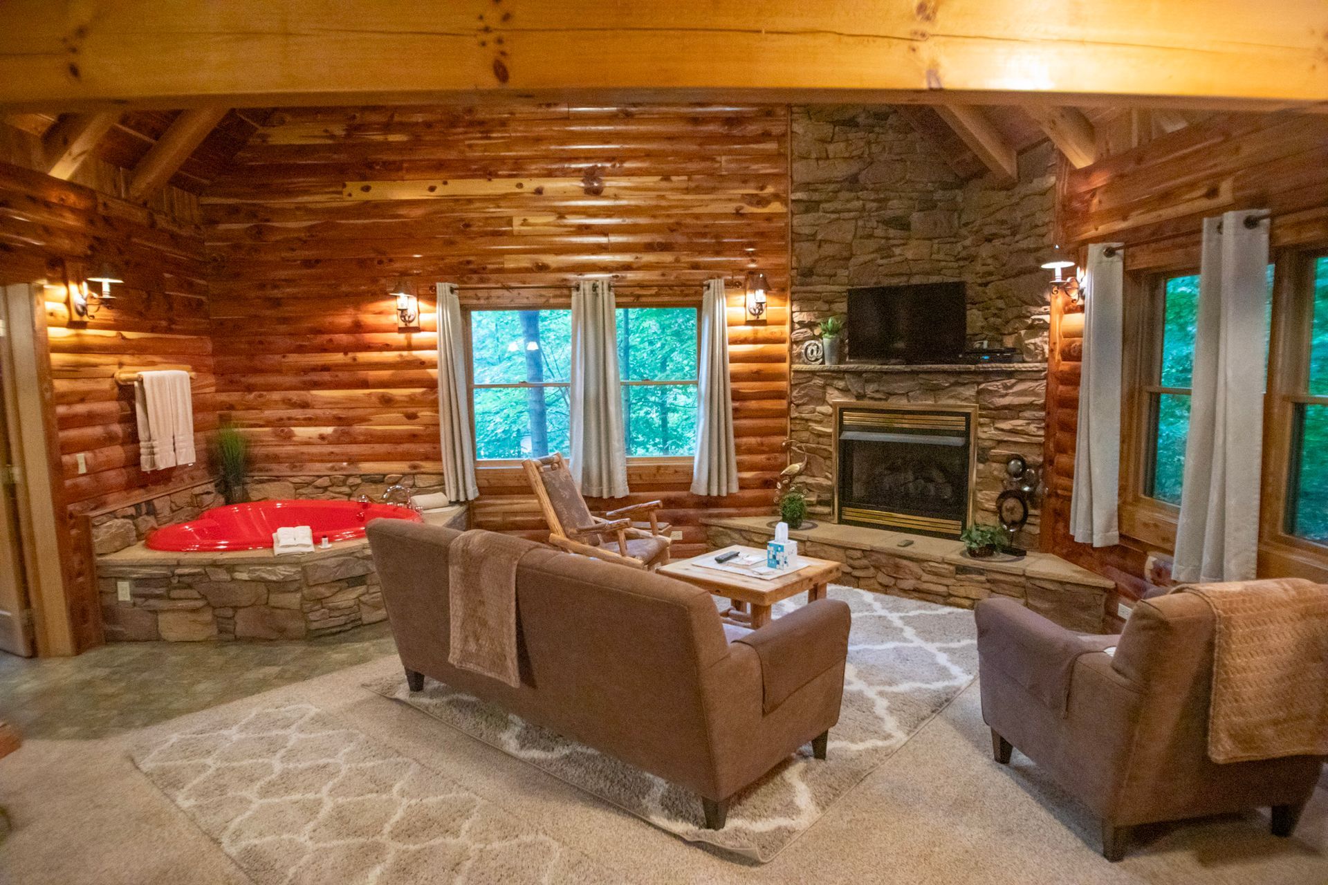 Cozy cabin interior with a fireplace, hot tub, and seating area. Wooden walls and natural light.