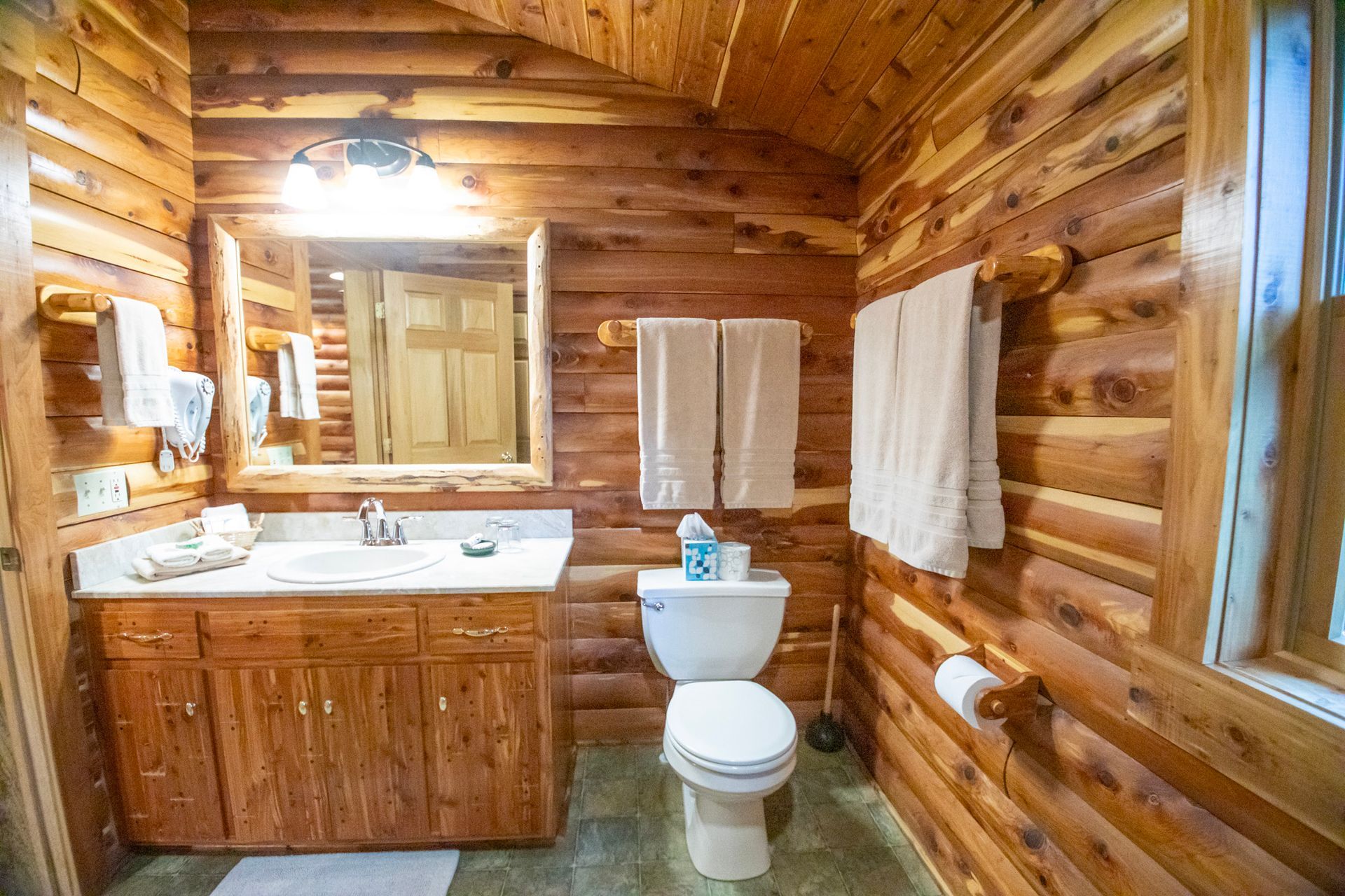 Rustic wooden bathroom with vanity, toilet, and towel racks.